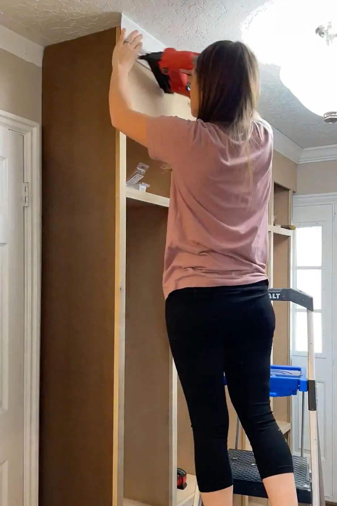 A DIYer securing crown molding to the top of custom-built mudroom lockers, giving them a polished, built-in look.